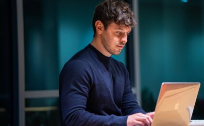 man wearing blue sweater writing on laptop